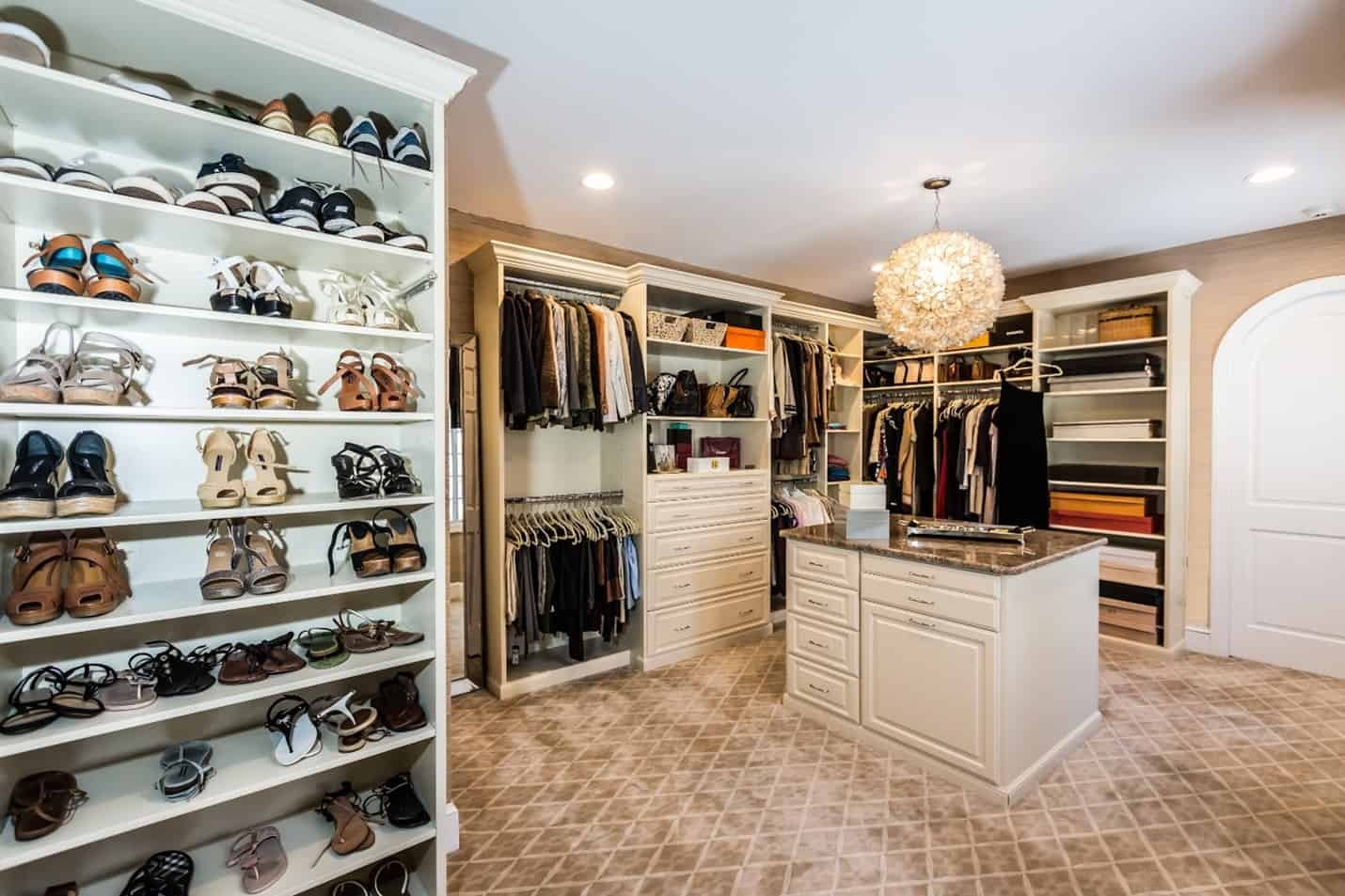 A grand walk-in closet with a shoe rack and island.